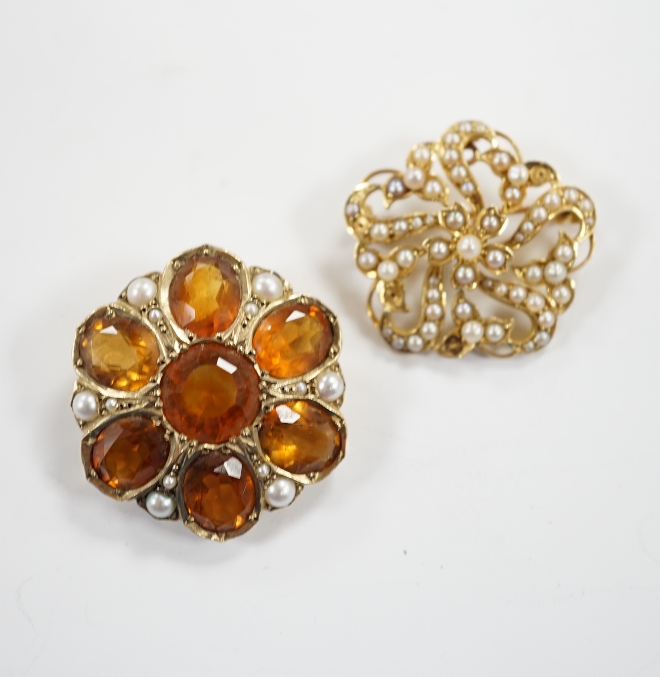 An early 20th century yellow metal, citrine and split pearl cluster set shaped circular brooch, 28mm and a similar 15ct and seed pearl cluster set brooch, gross weight 18.5 grams.